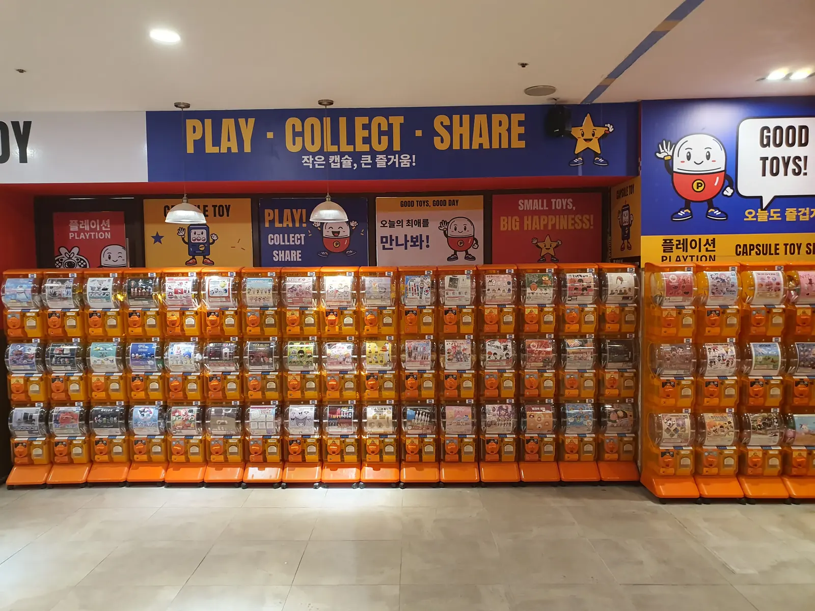 PLAY · COLLECT · SHARE 문구가 적힌 파란 벽 아래로 주황색 캡슐토이 기기가 줄지어 있는 매장 내부
